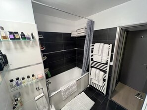 A modern bathroom with a bathtub, a shower area, and a glass shelf with toiletries.