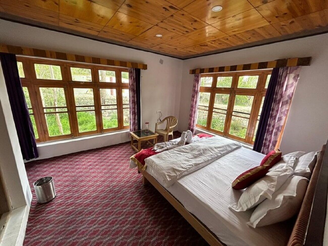 A bedroom with a large bed, two windows, a chair, and a small table.