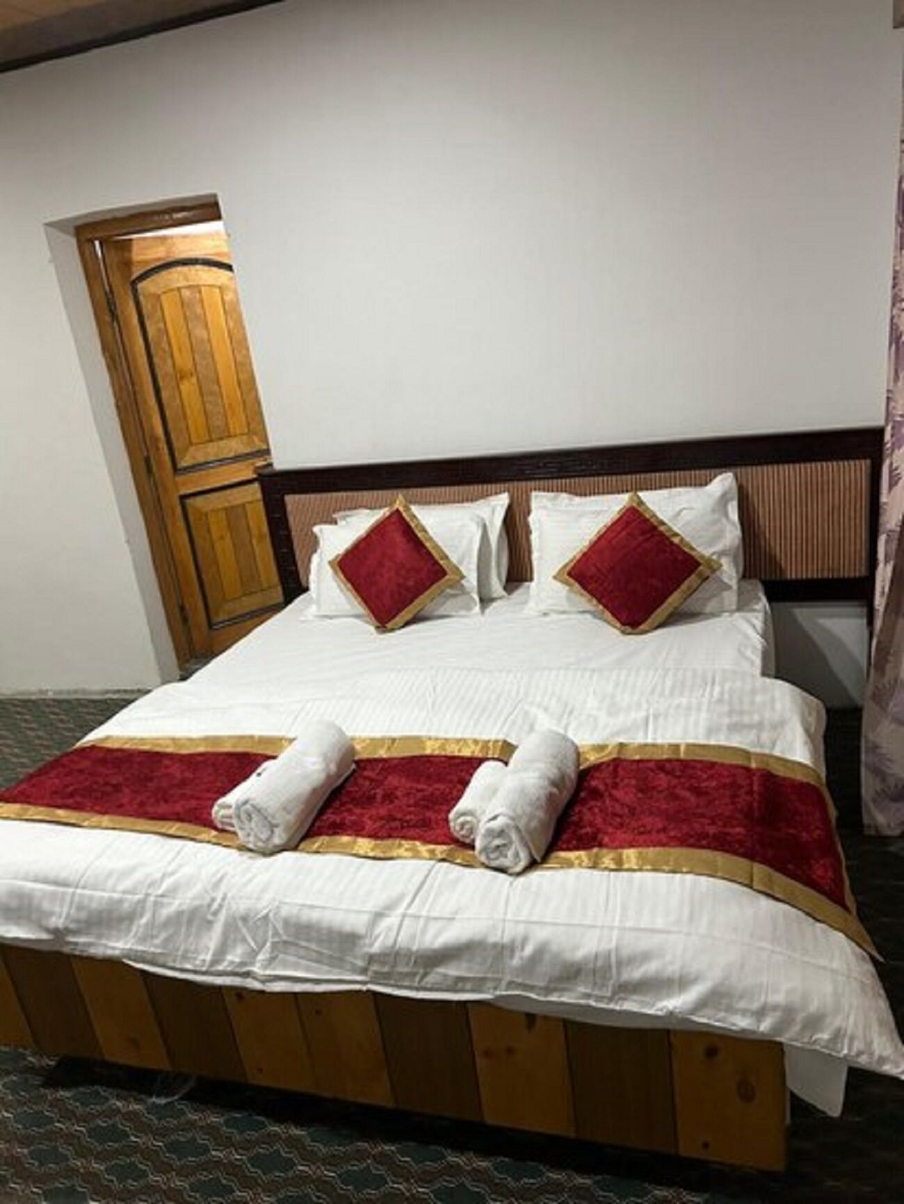 A neatly made bed with white linens, red pillows, and a red and gold bedspread.