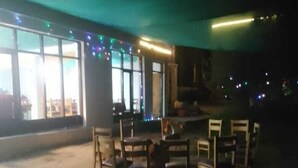 Un espace de restauration en plein air avec une table ronde et des chaises, entouré de fenêtres décorées de guirlandes lumineuses.