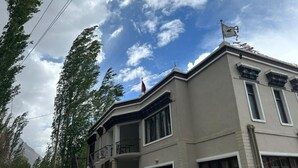 Un bâtiment à deux étages, doté d’un balcon au deuxième étage, d’un drapeau au sommet et ayant une chaîne de montagnes en arrière-plan.