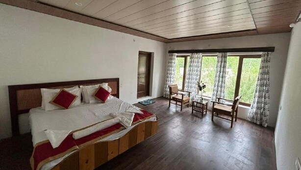 Une chambre à coucher avec un lit en bois, une petite table et une chaise près d’une fenêtre ornée de rideaux.