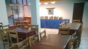 Un espace repas avec plusieurs tables et chaises, une table recouverte d’une nappe bleue au centre, et un comptoir derrière lequel se trouve une personne.