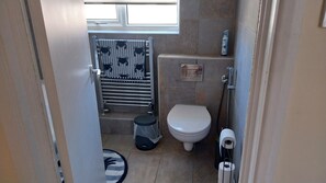 A small bathroom with a toilet, a towel rack with striped towels, a shower area, and a toilet paper holder. - Beautiful 3-bed Bungalow Kessingland Rural Retreat (Lowestoft)