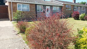 A residential house with a brick exterior, a tiled roof, and a front yard with various shrubs and a lawn. - Beautiful 3-bed Bungalow Kessingland Rural Retreat (Lowestoft)