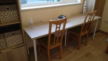 A small dining area with a white table and two wooden chairs, a window with a view of the outside, and a patterned storage unit to the left.