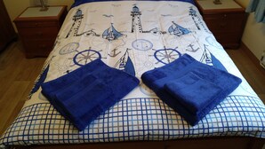 Ein ordentlich gemachtes Bett mit einem wellen-inspirierten Bettbezug, zwei passende Kissen und zwei gefaltete Handtücher auf dem Bett.