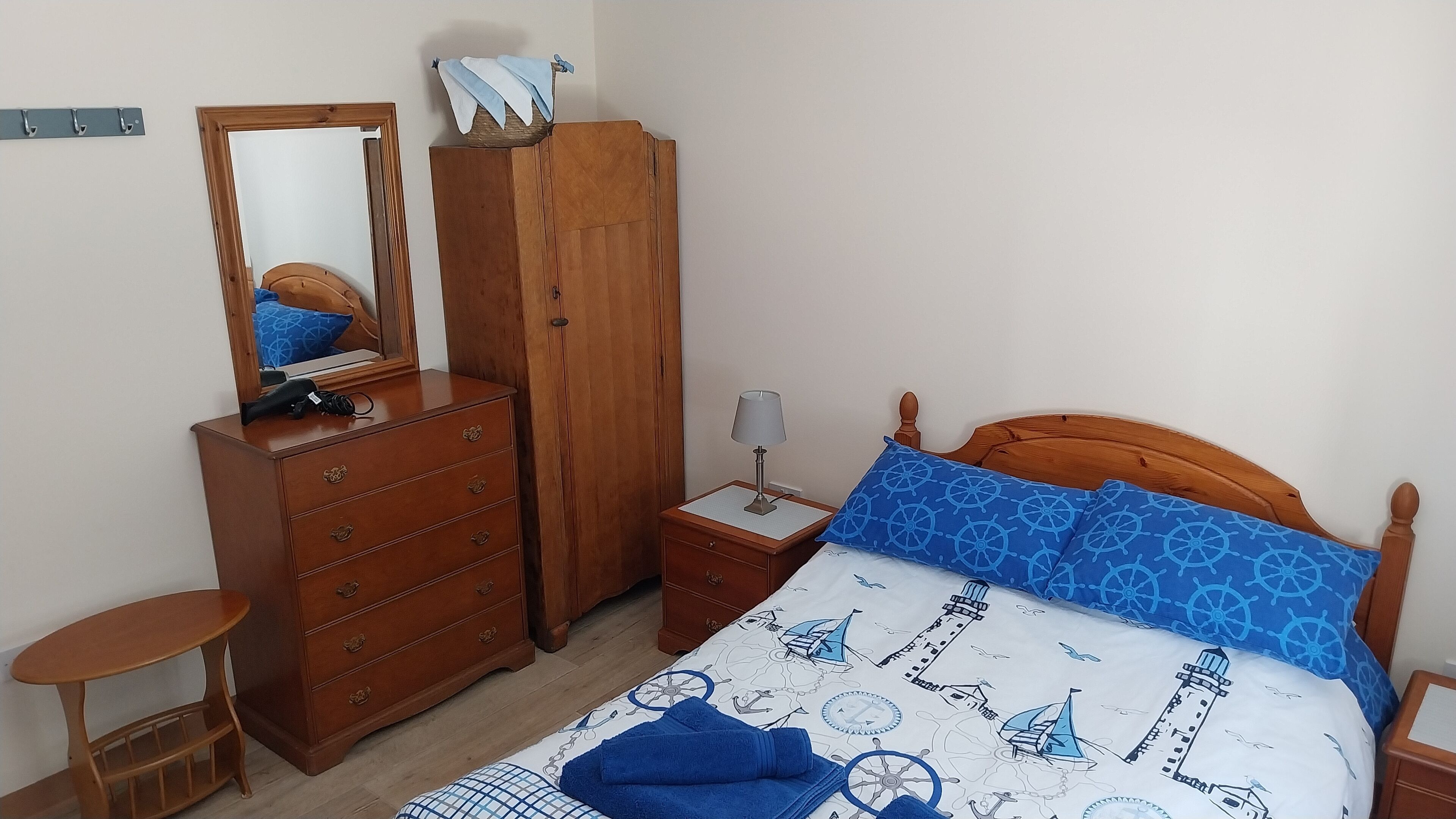 Ein Schlafzimmer mit einem hölzernen Bett, einem Nachttisch mit Lampe, einer Kommode mit Spiegel und einem kleinen Tisch.