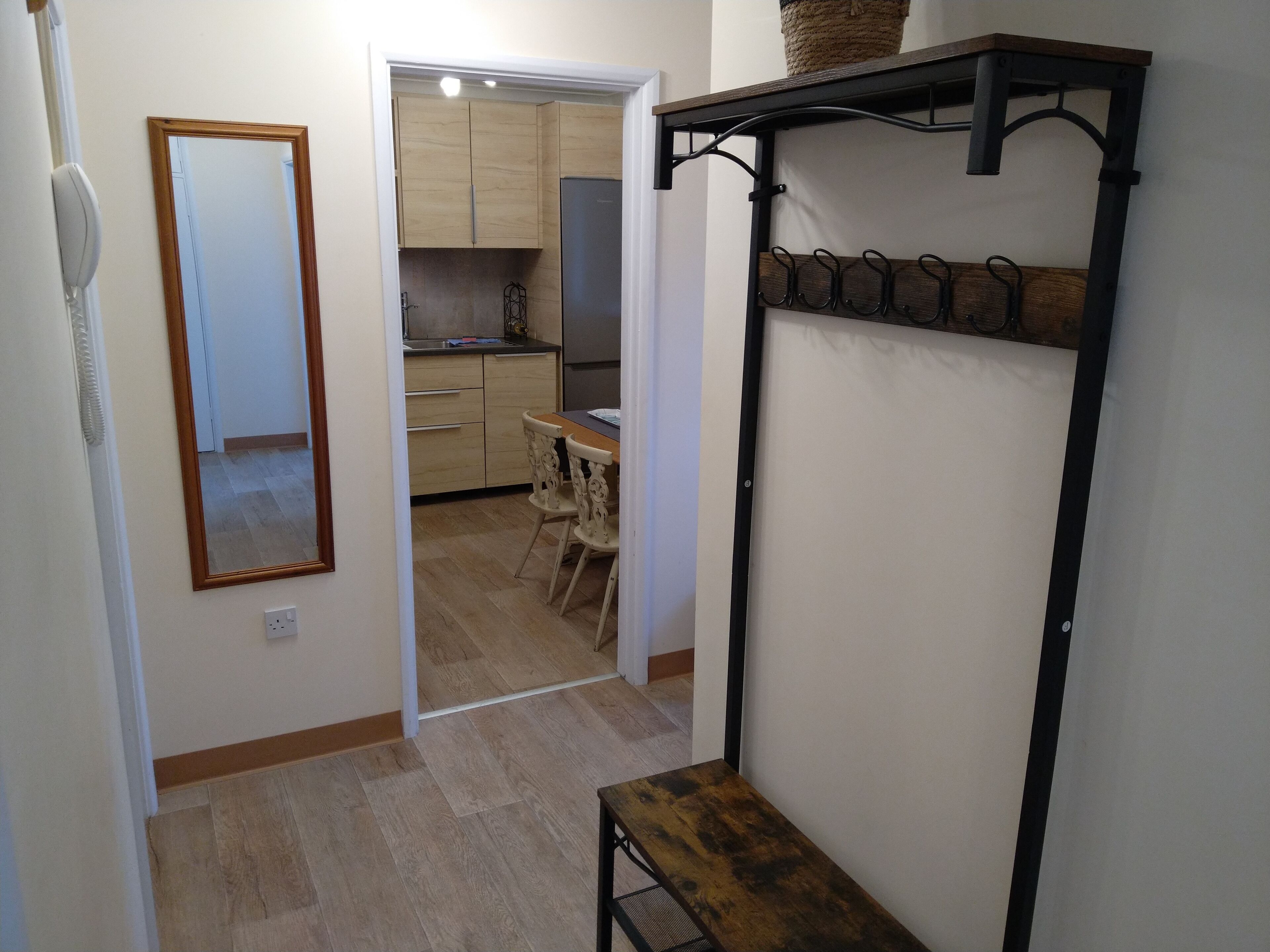A hallway with a wooden bench, a mirror, and a kitchen area visible through an open door.