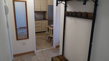 A hallway with a wooden bench, a mirror, and a kitchen area visible through an open door.