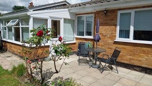 Eine Terrasse mit Tisch und Stühlen, ein Rosengarten und eine Backsteinmauer.