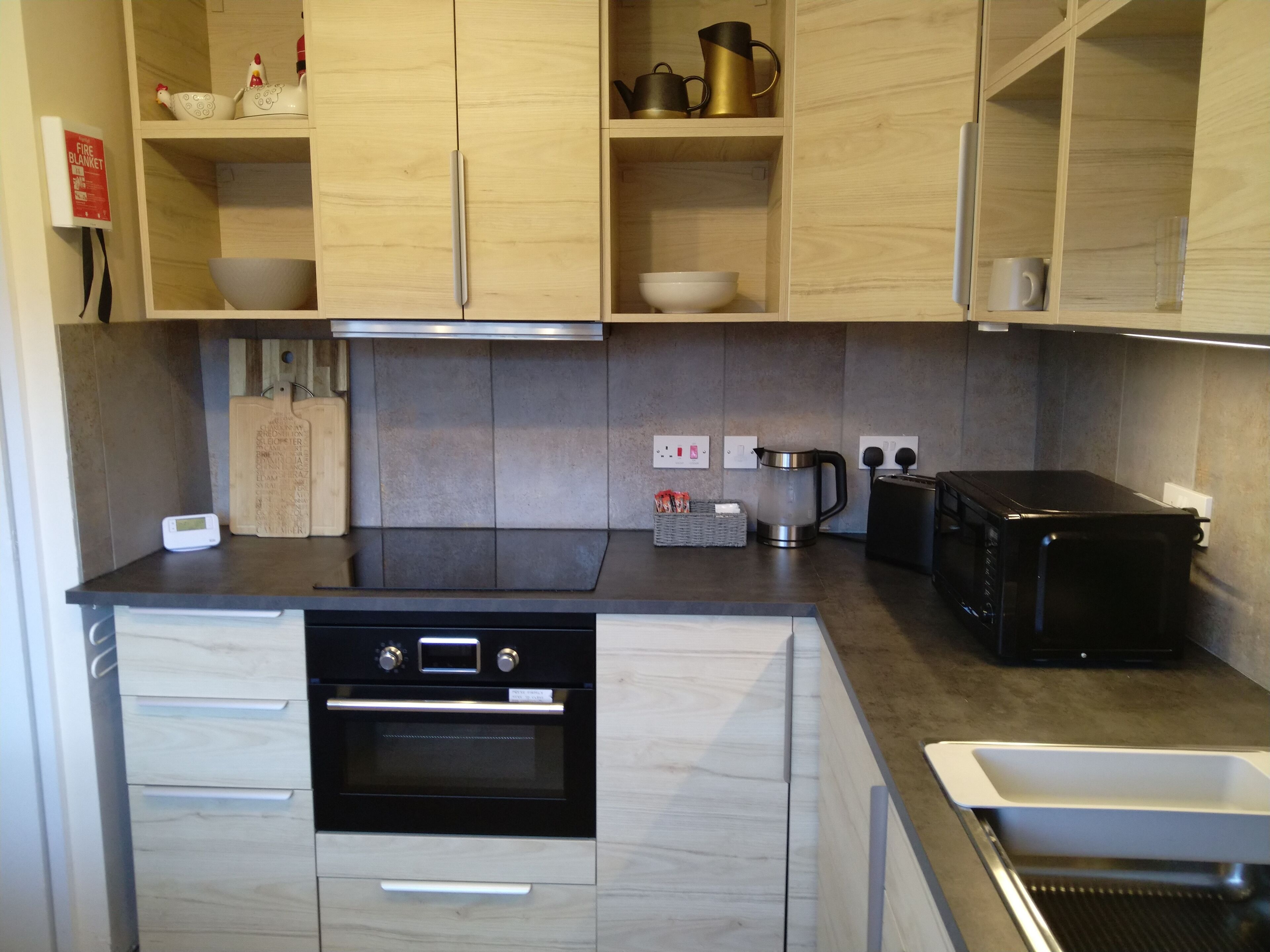 A modern kitchen with wooden cabinets, a built-in oven, a coffee maker, and a toaster.
