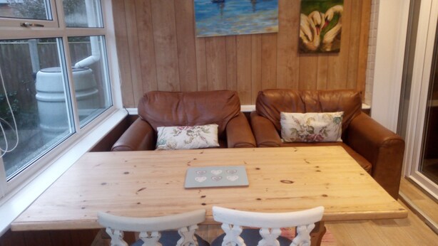Ein gemütlicher Raum mit Holzwand, braunem Ledersofa, Holztisch und weißem Stuhl.