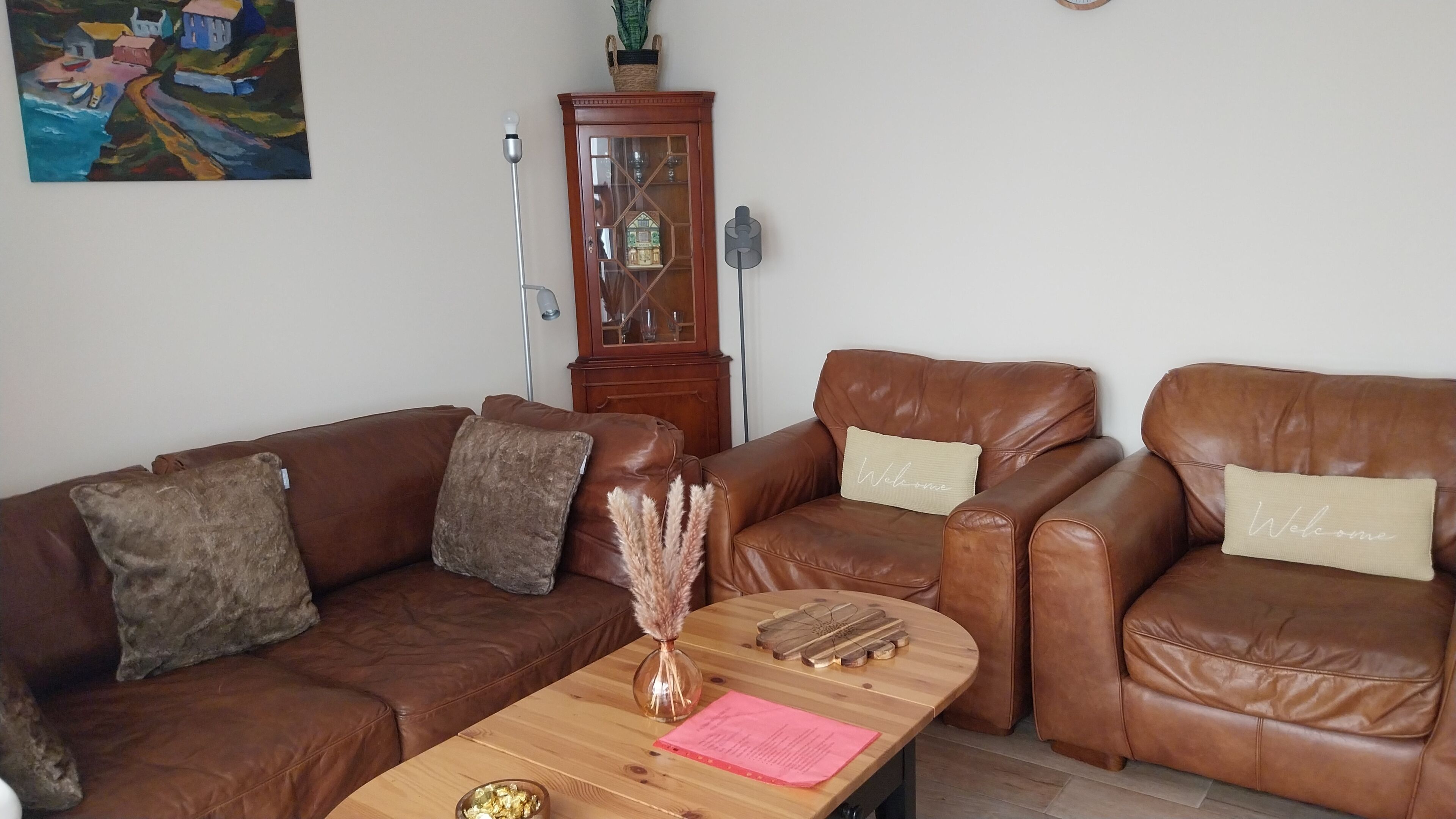 A living room with two brown leather sofas, a wooden coffee table with decorative items, and a wooden cabinet with glass doors.