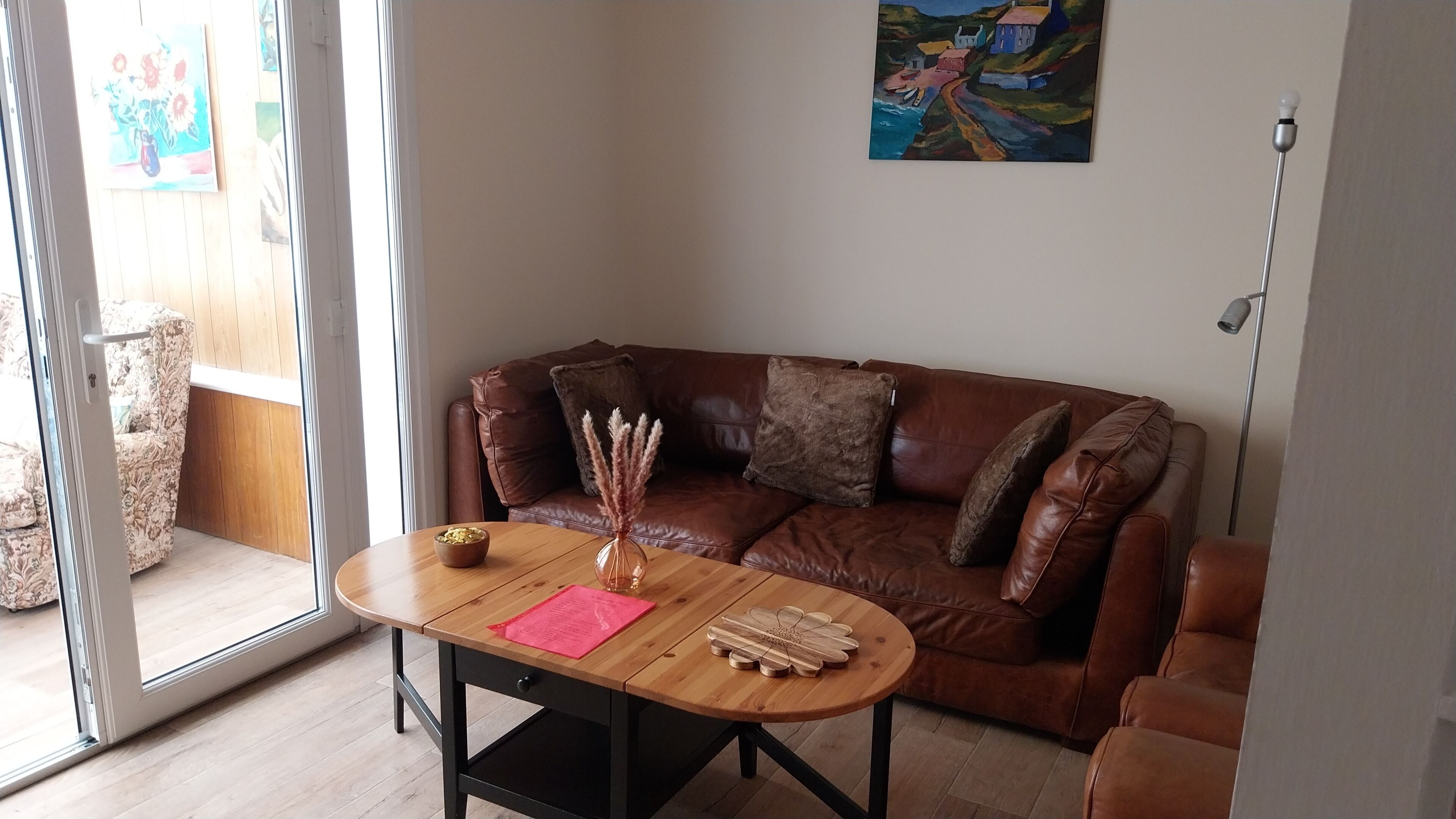 Ein Wohnzimmer mit einem braunen Ledersofa, einem Couchtisch mit einer Vase und einer Blume sowie einem Bild an der Wand.