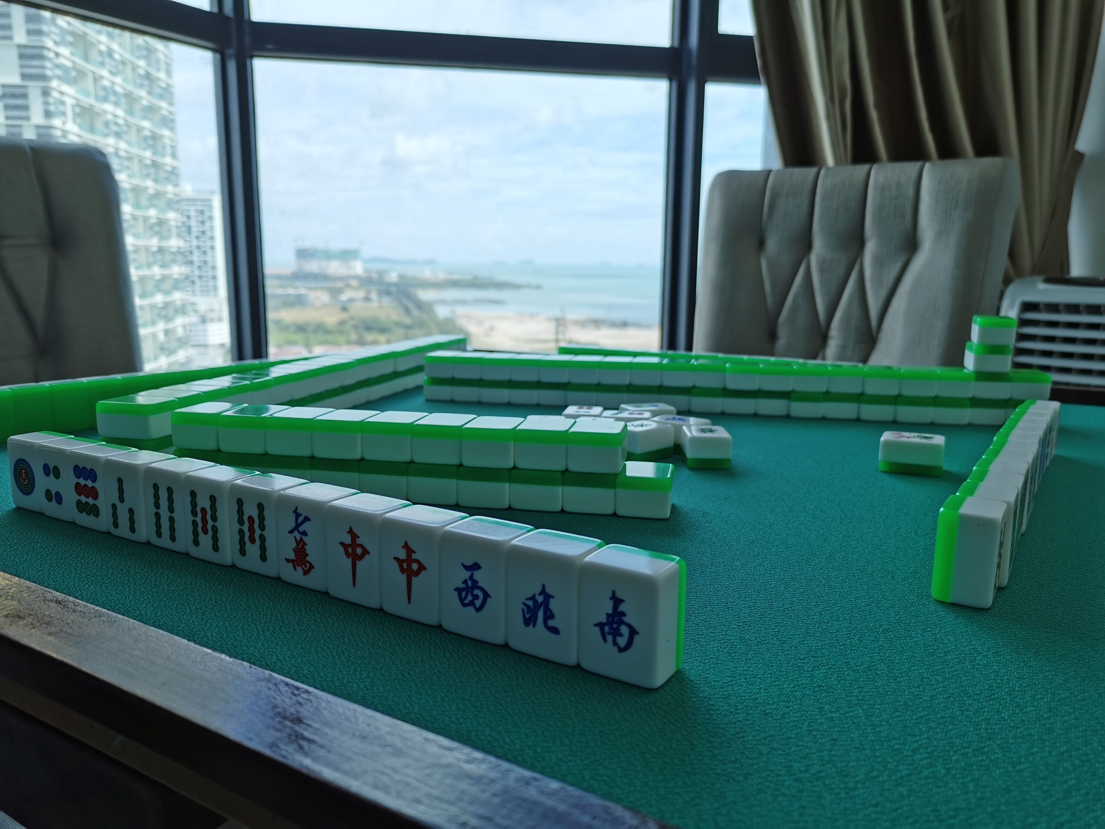 A mahjong table set up indoors with a view of a cityscape through large windows.