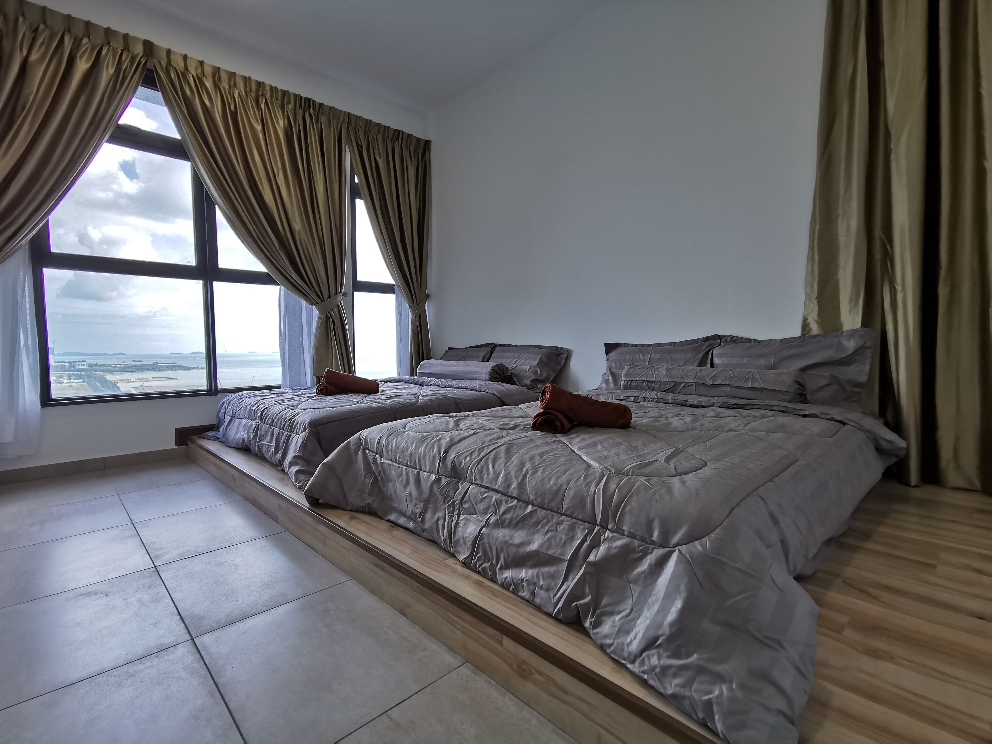 Una habitación de hotel moderna con dos camas, ventanas amplias y vista al mar.