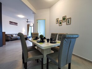 A dining area with a table set for four, surrounded by upholstered chairs. A ceiling fan is visible in the background, and there are framed botanical prints on the wall.