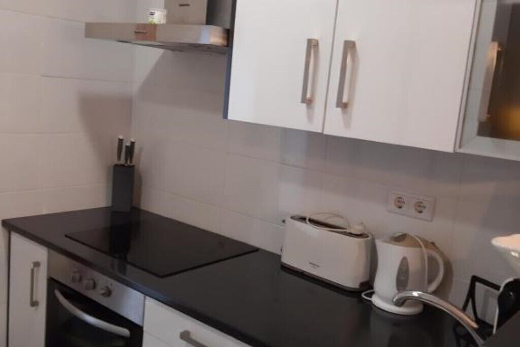 A compact kitchen with white cabinets, a black countertop, a built-in oven, a toaster, and a kettle.