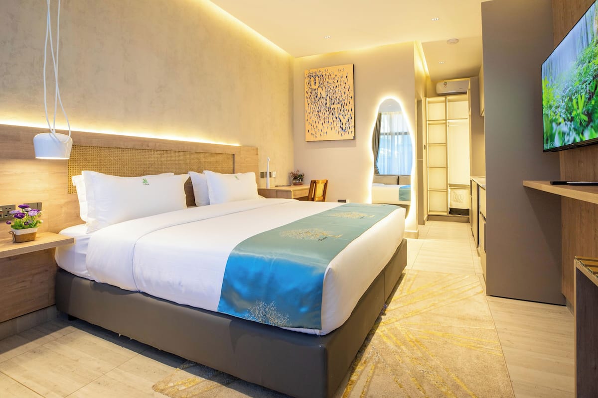 Une chambre d’hôtel moderne dotée d’un grand lit, de tables de chevet, d’un téléviseur à écran plat et d’un dressing.