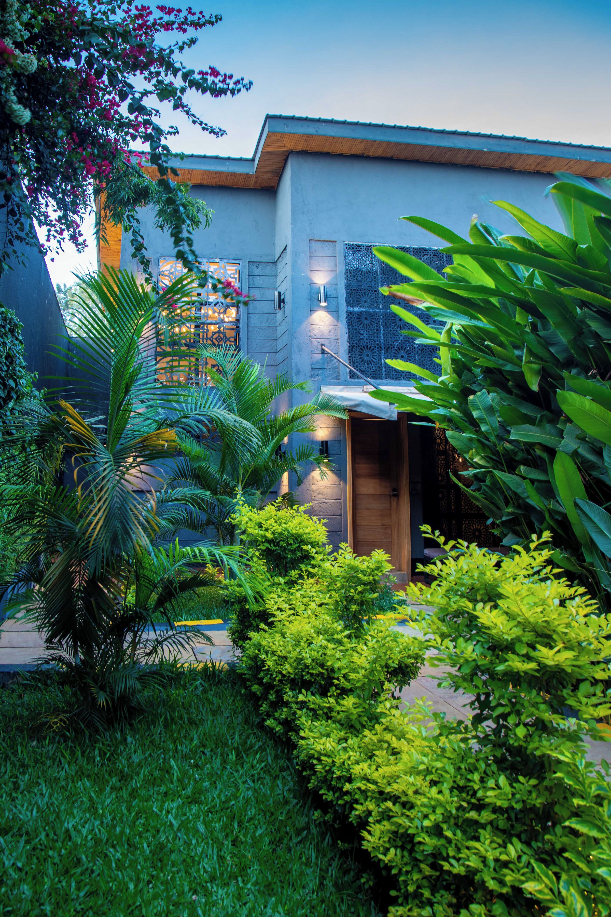 A modern building with a well-maintained garden, including various plants and a pathway leading to the entrance.