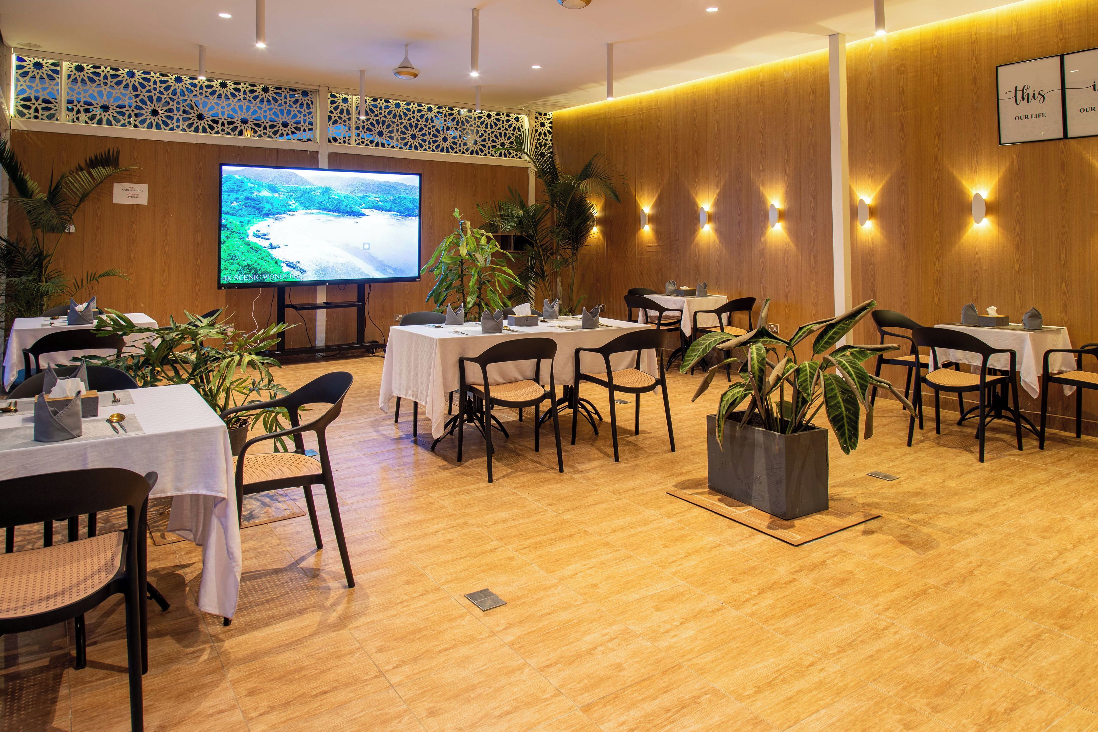 A conference room with tables and chairs, a large screen, and decorative plants.