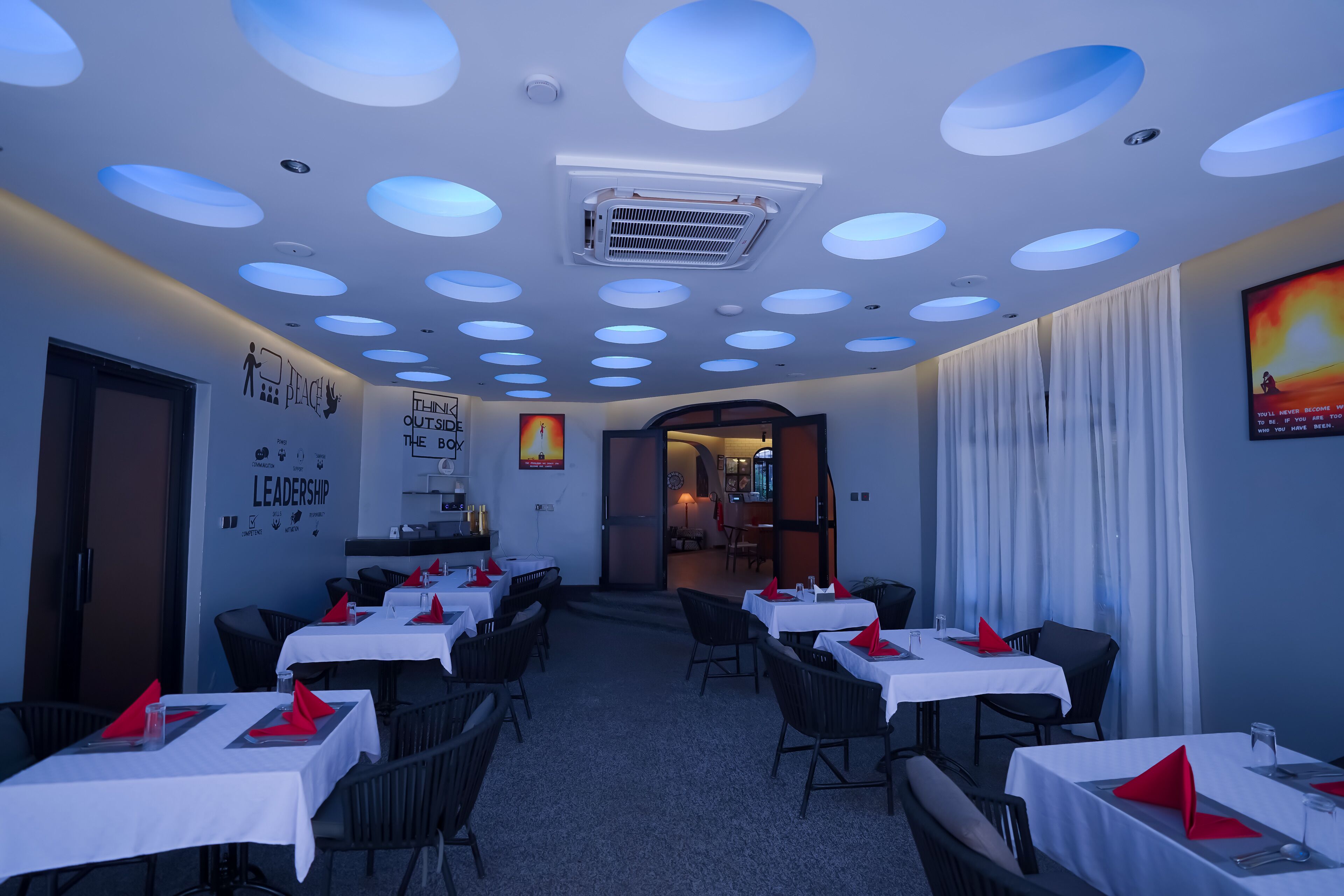 A restaurant with round ceiling lights, white tables, and black chairs.