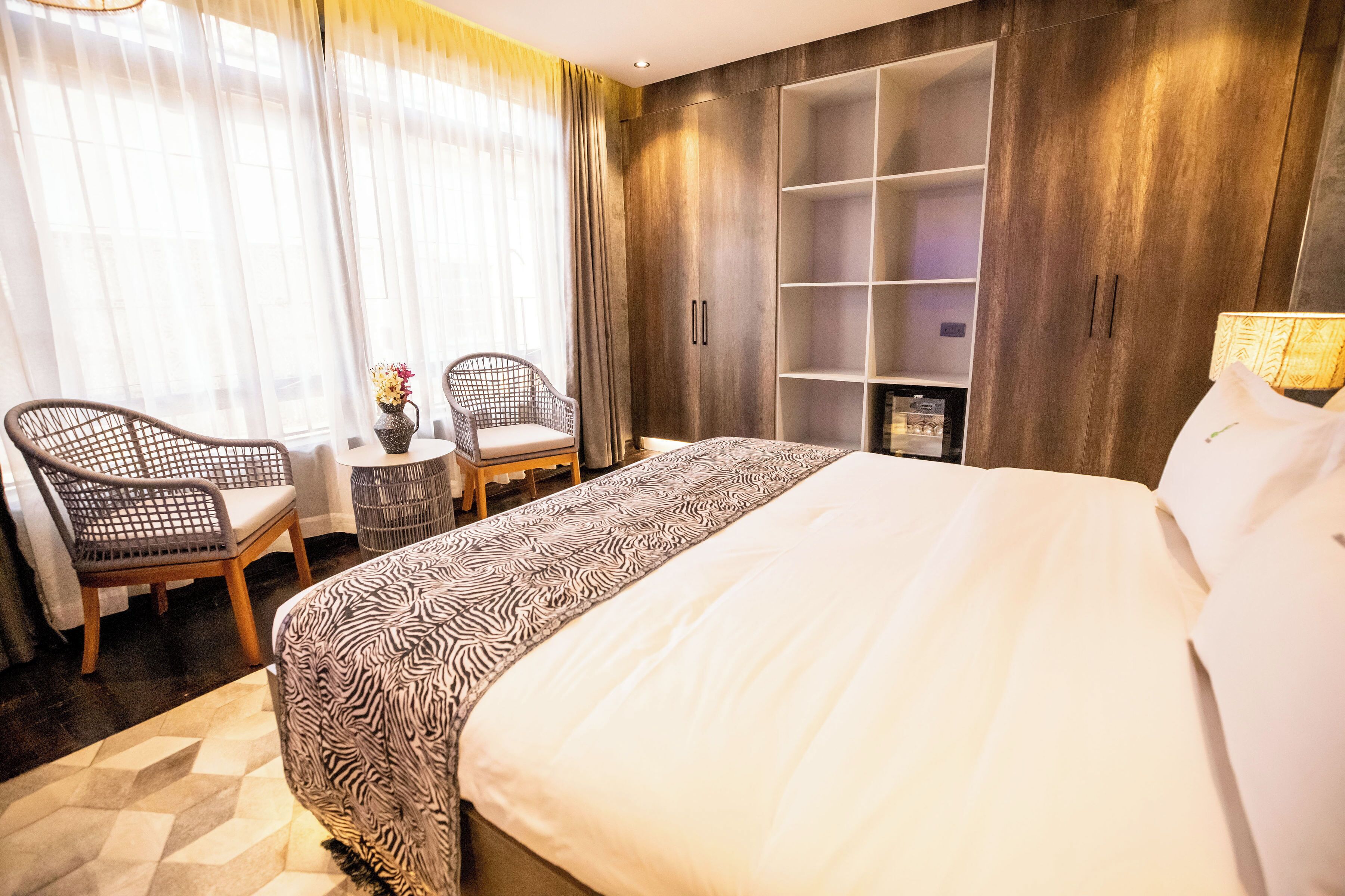 Et hotelværelse med en stor seng, to stole, et lille bord med en vase og et garderobeskab med hylder.