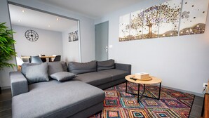 A modern living room with a grey sectional sofa, a small round table, and a colorful geometric rug. - Résidence Hermès Paris Orly Aéroport (Villeneuve-le-Roi)