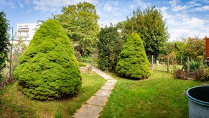 A garden with a stone pathway, neatly trimmed coniferous trees, and a metal barrel. - Résidence Hermès Paris Orly Aéroport (Villeneuve-le-Roi)