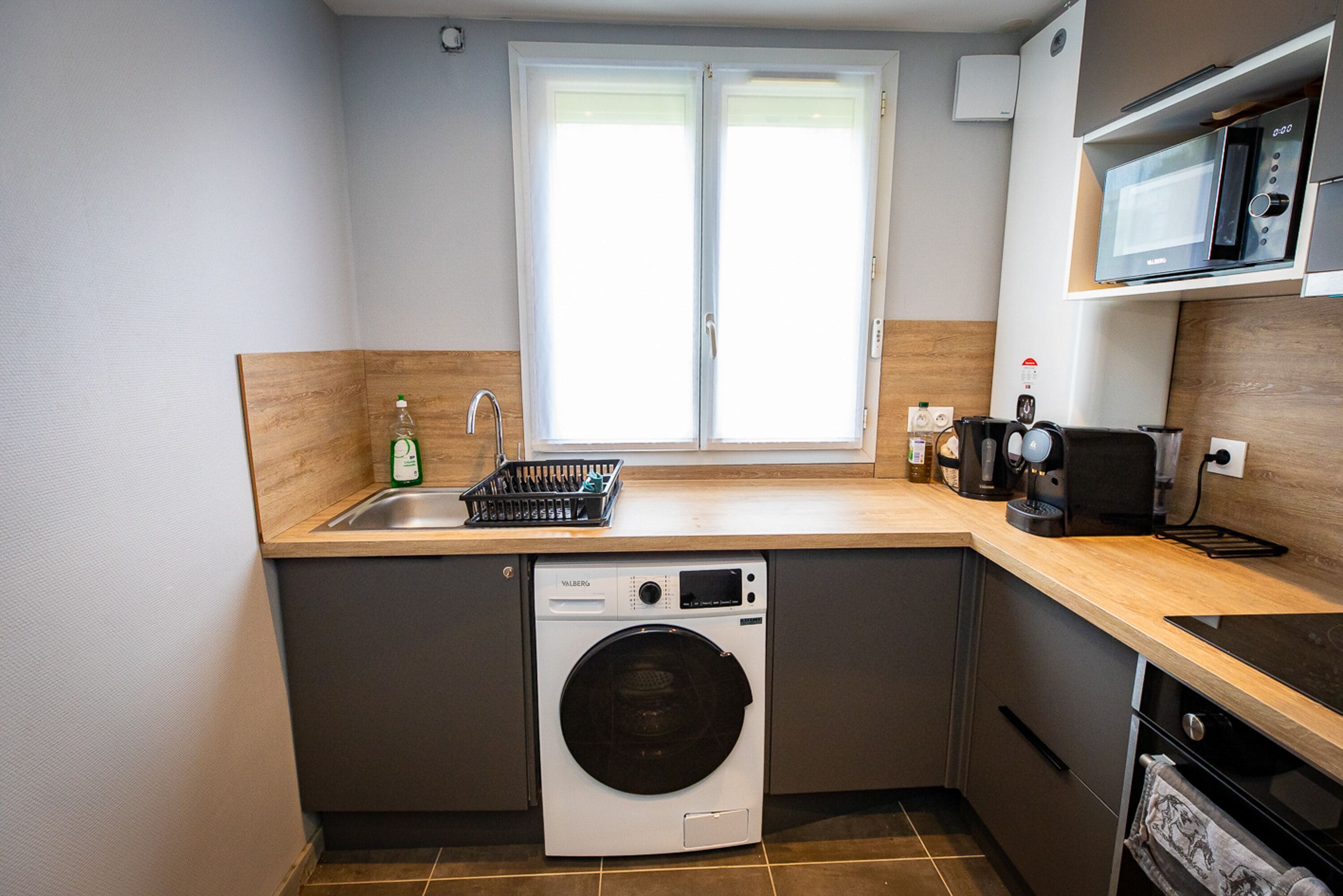 A compact kitchen with a washing machine, a sink, a microwave, and a coffee maker.