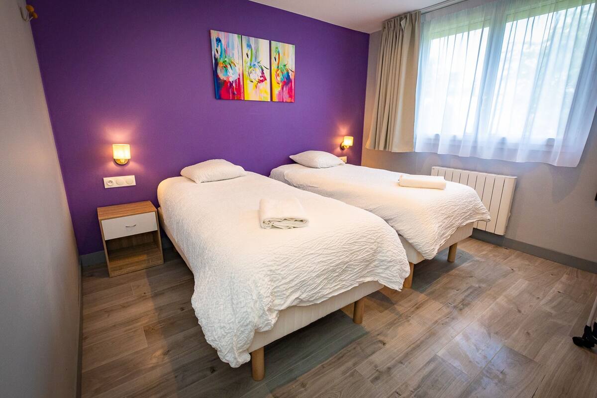 A room with two beds, purple walls, and a window with curtains.