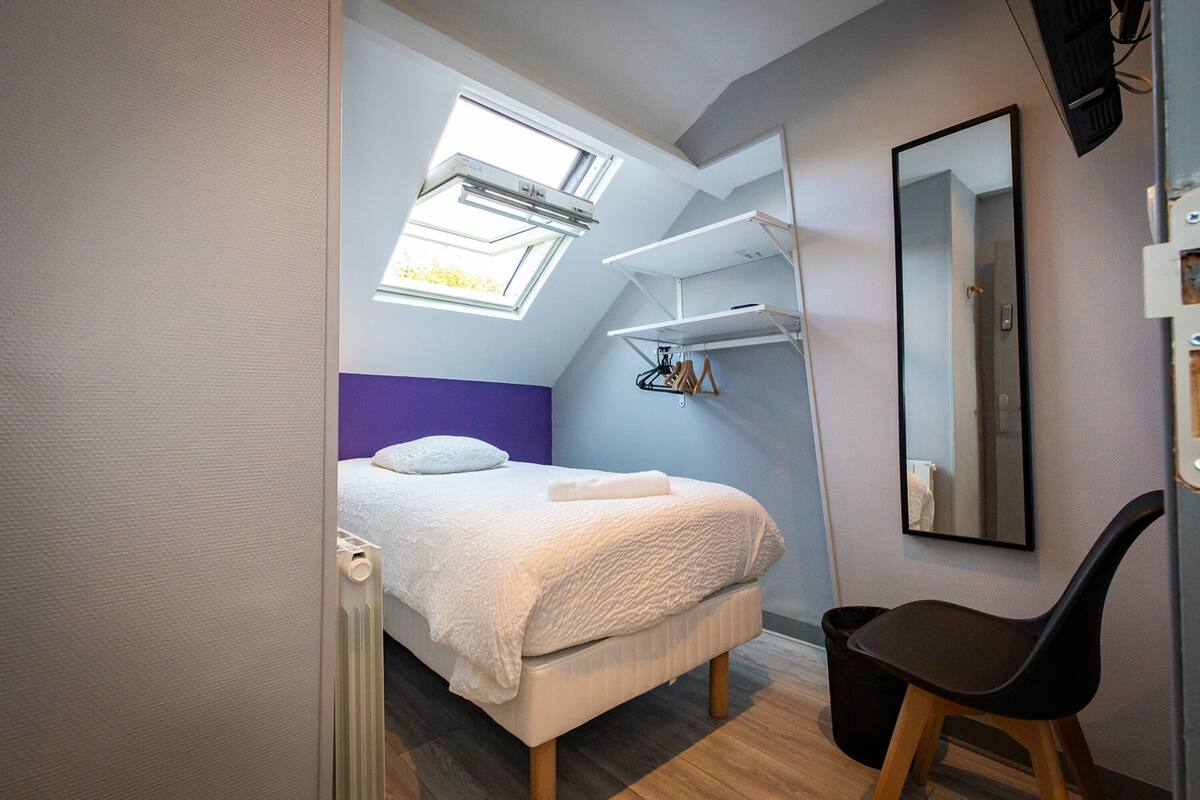A bedroom with a bed, a chair, a mirror, and built-in shelves.