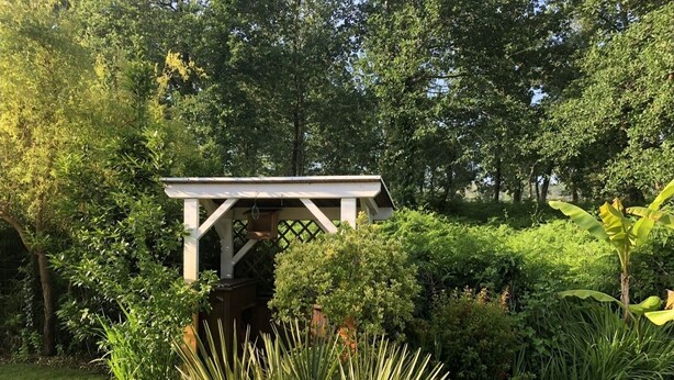 A garden with a white pergola structure surrounded by lush greenery and various plants. - 4 bedroom villa with swimming pool, in a large lush garden, 3km from the beaches (Messanges)