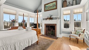 Un dormitorio amplio con una cama grande, chimenea y varias ventanas con vistas al exterior.