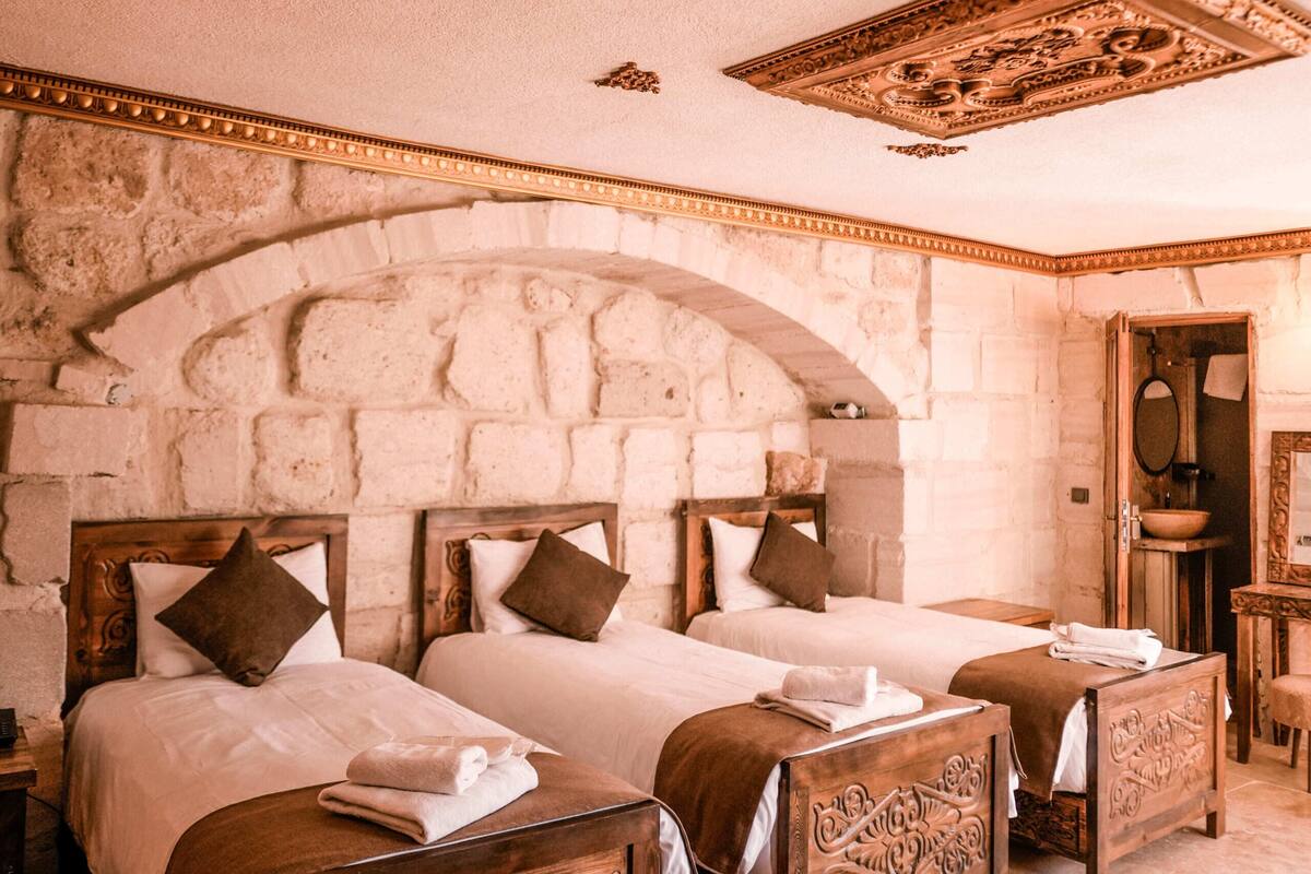 Una habitació amb dos llits de fusta, parets de pedra i un sostre decoratiu.