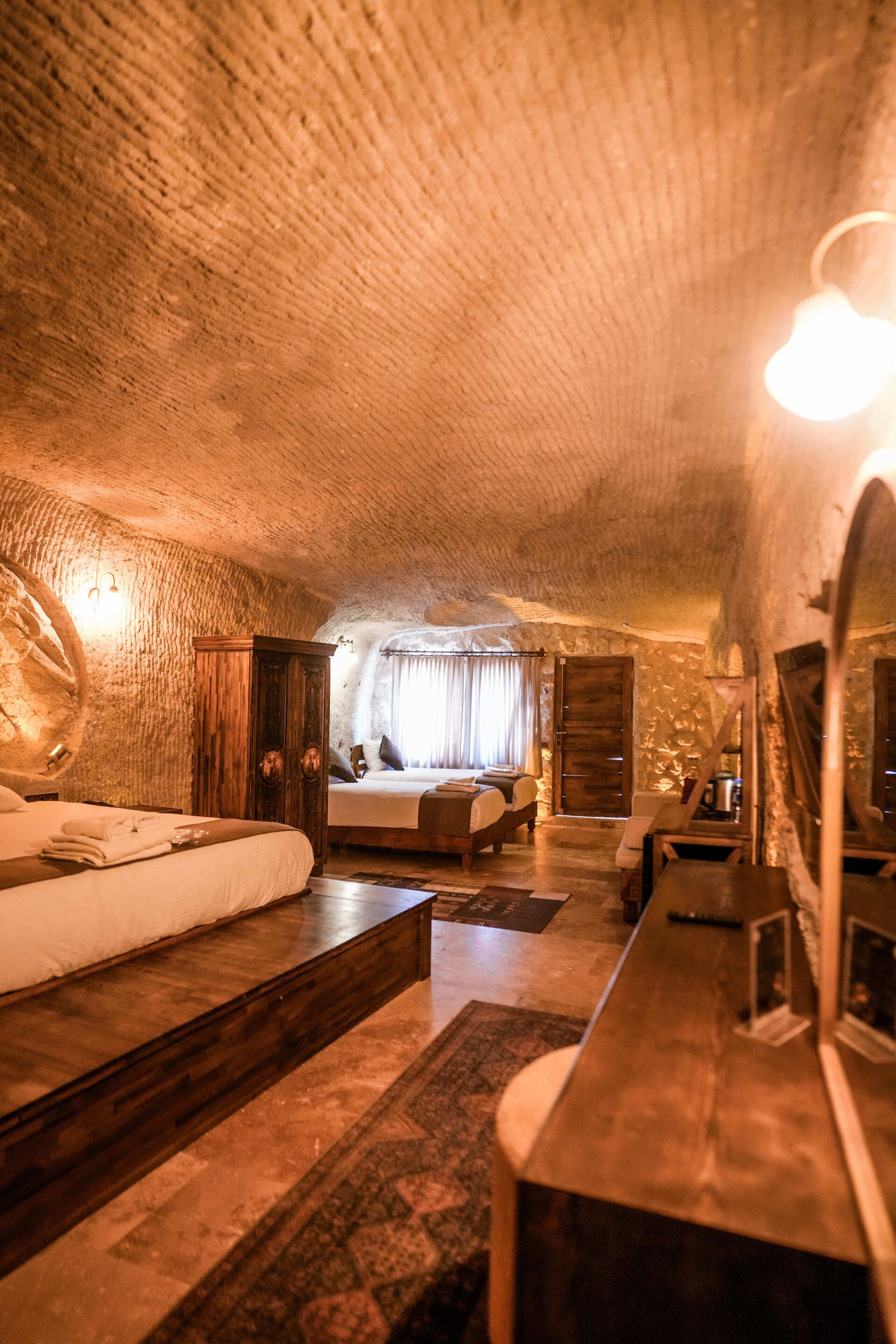 A cozy, rustic room with a stone ceiling, a bed, a desk, and a large mirror.