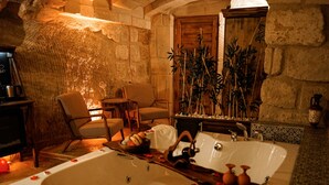 Casa de banho com paredes de pedra, banheira independente, soalho de madeira e um espaço de estar com cadeiras e uma mesa.