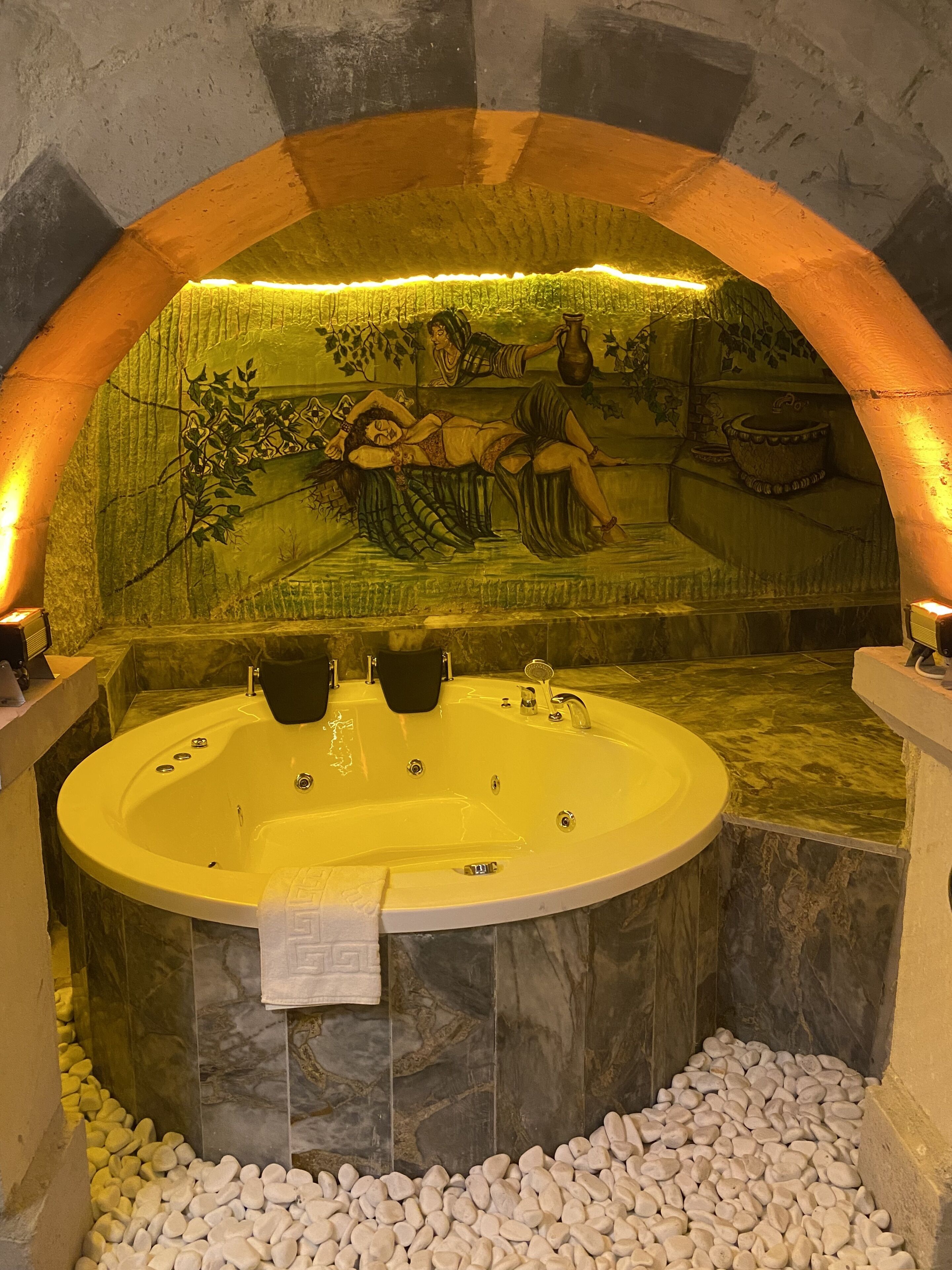 A spa area with a large bathtub, a mural, and a stone wall.