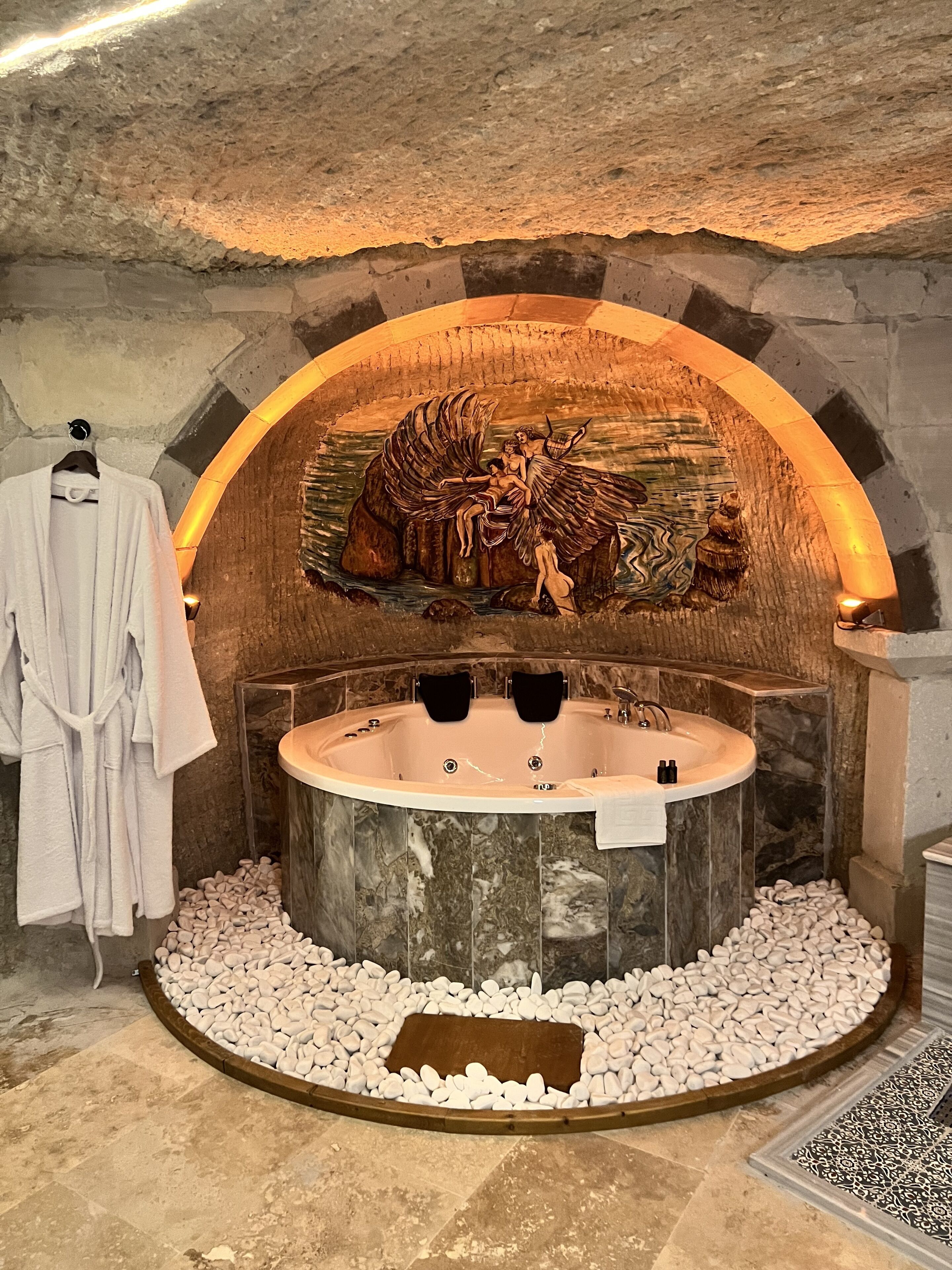 A spa area with a stone wall, a hot tub, and a pebbled floor.