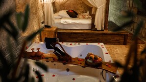 Quarto com uma banheira grande, cama com cortinas brancas e parede de pedra.