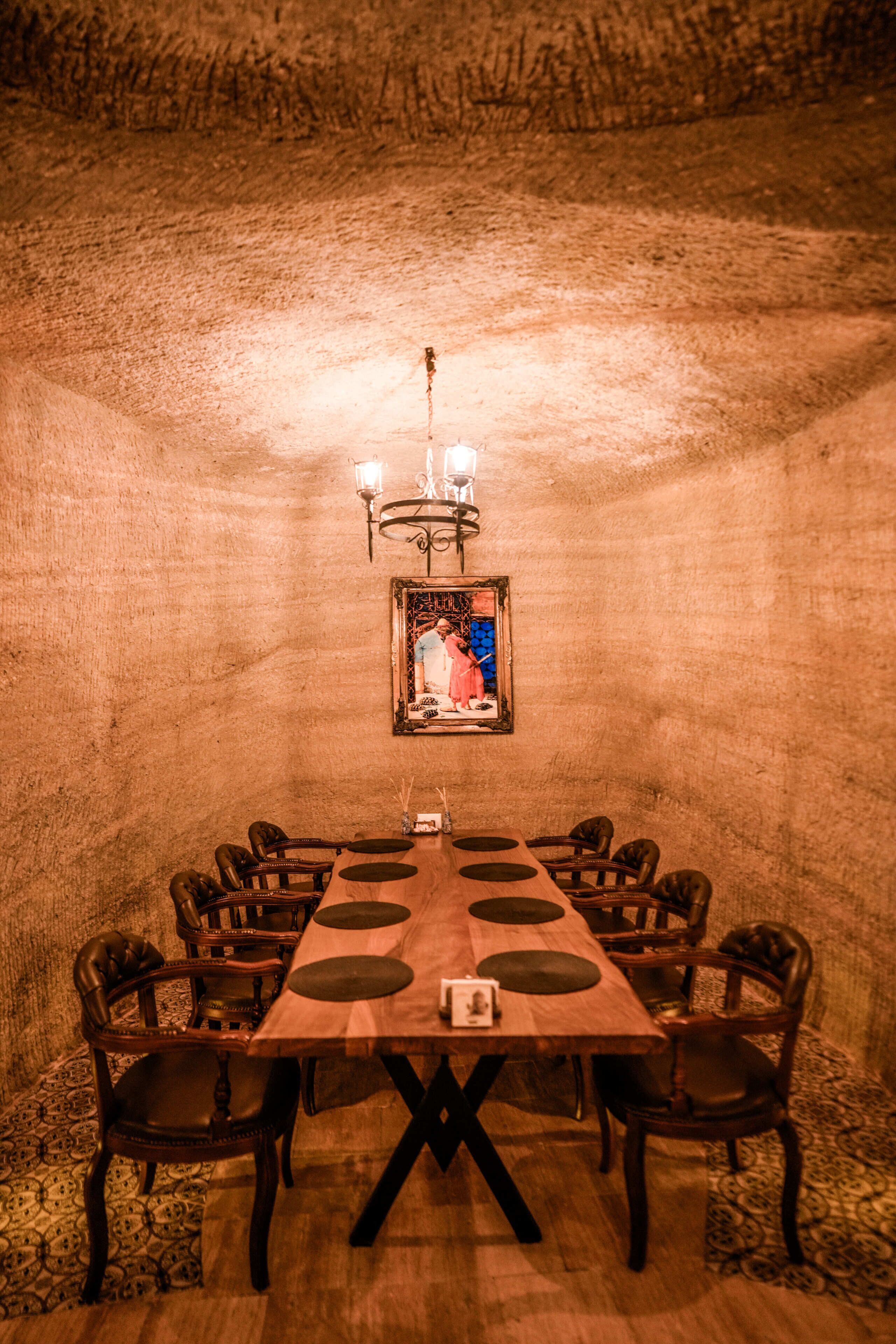 Une salle de conférence avec une longue table, des chaises, un lustre et un tableau encadré au mur.