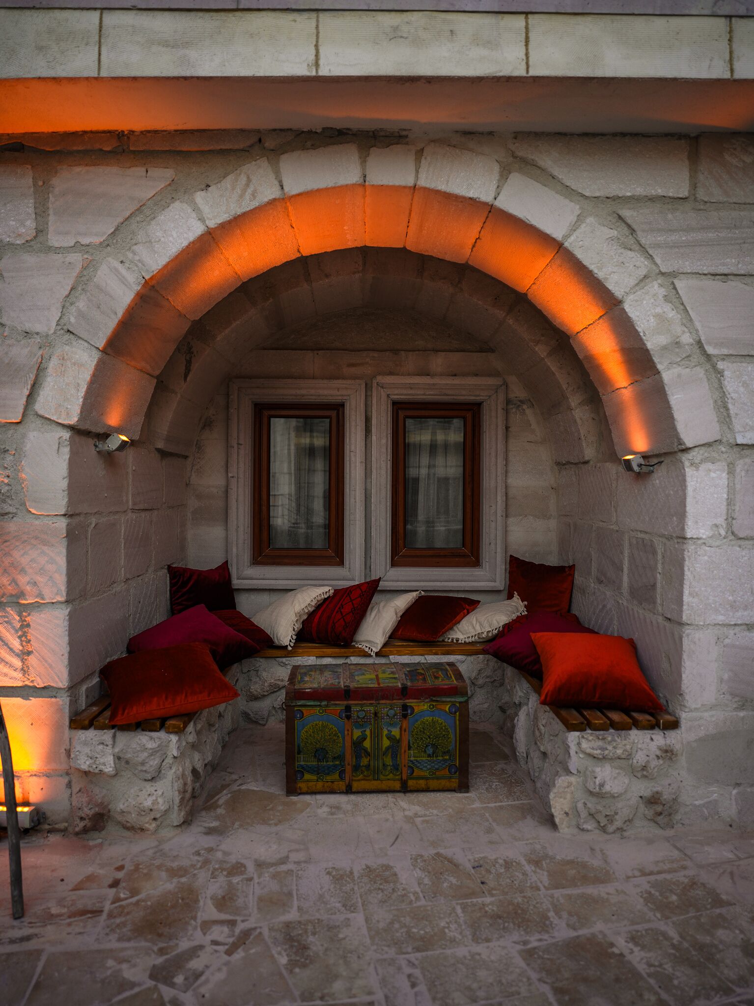 A stone bench with red cushions under a stone archway with two windows.