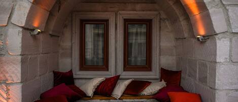 A stone bench with red cushions under a stone archway with two windows.