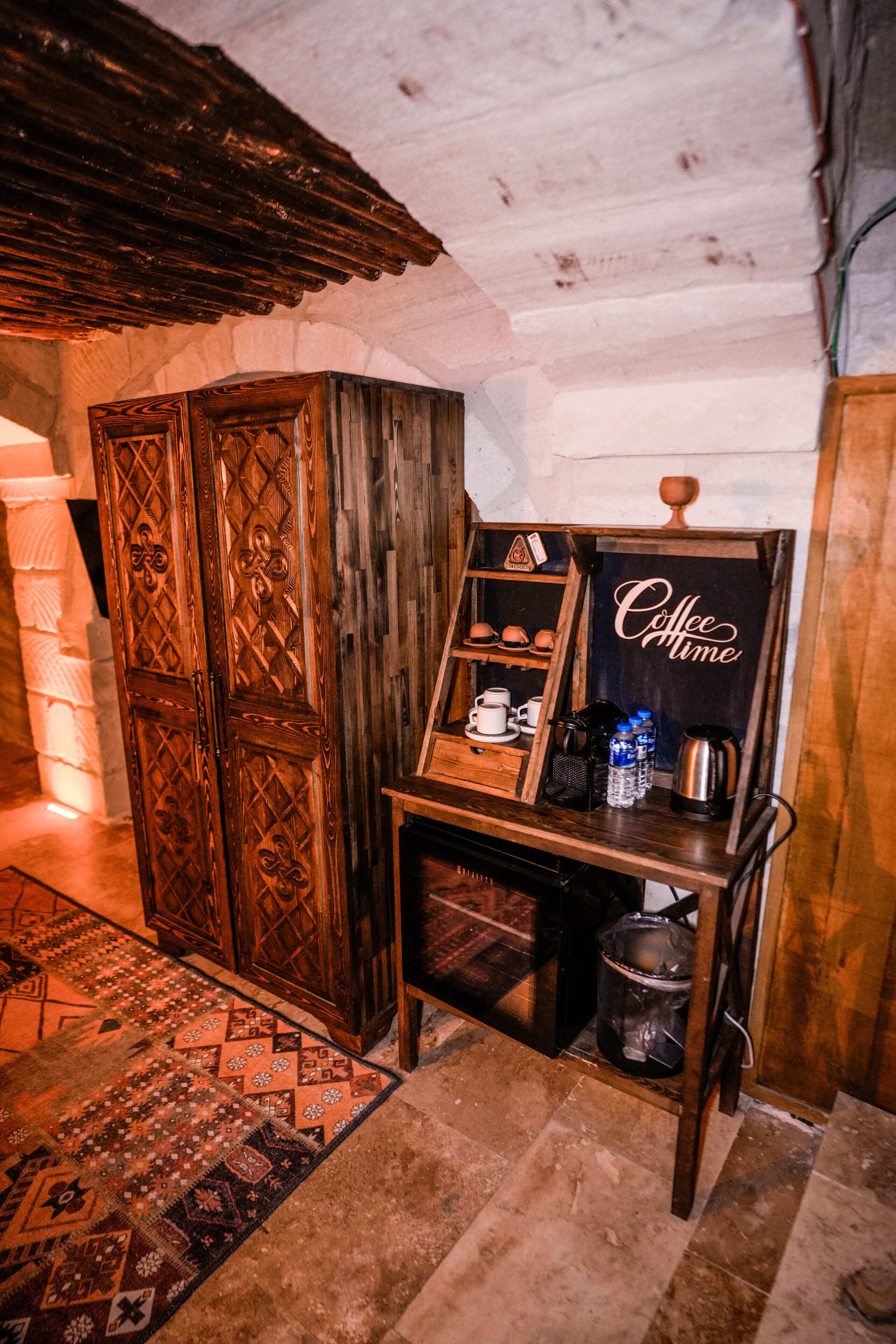 A rustic interior with a wooden cabinet, a coffee station, and a patterned rug.
