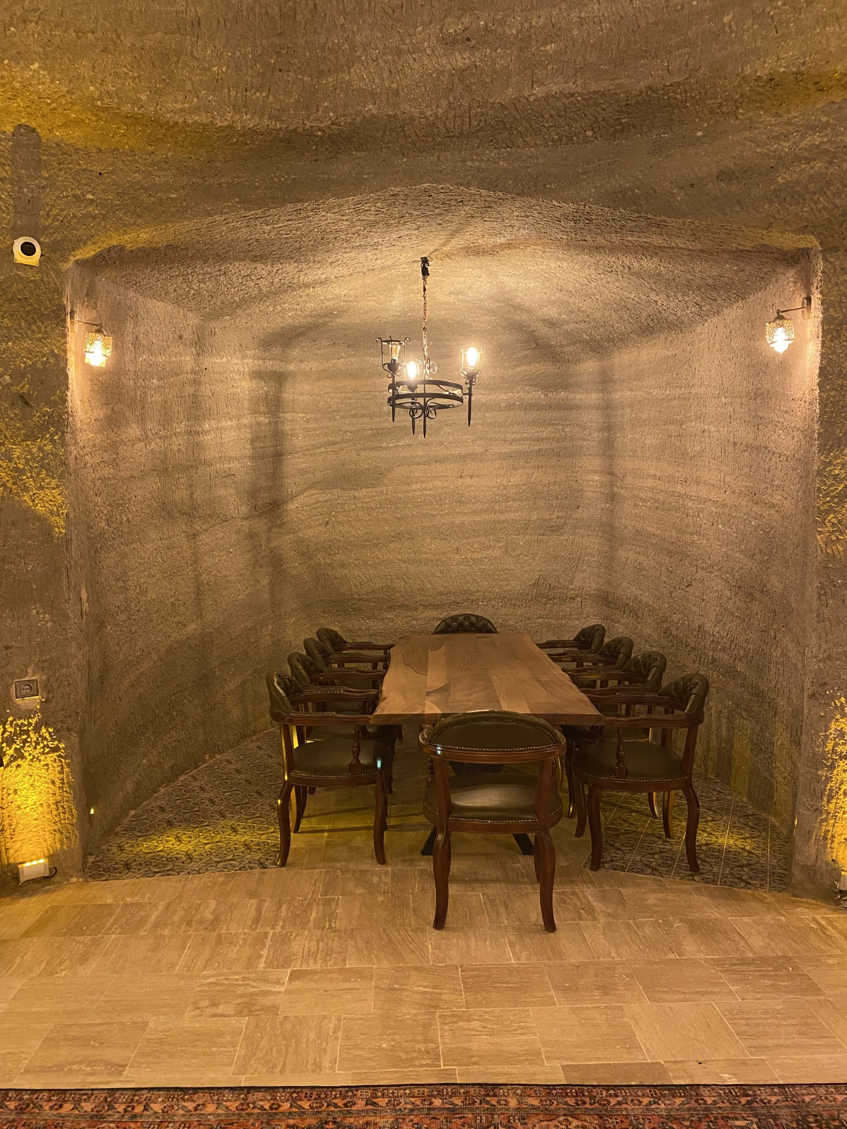 Un salón de conferencias con una larga mesa de madera, sillas de cuero, una araña y paredes de piedra.