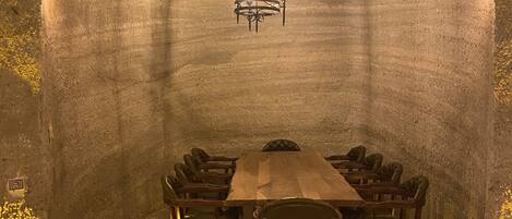 Un salón de conferencias con una larga mesa de madera, sillas de cuero, una araña y paredes de piedra.