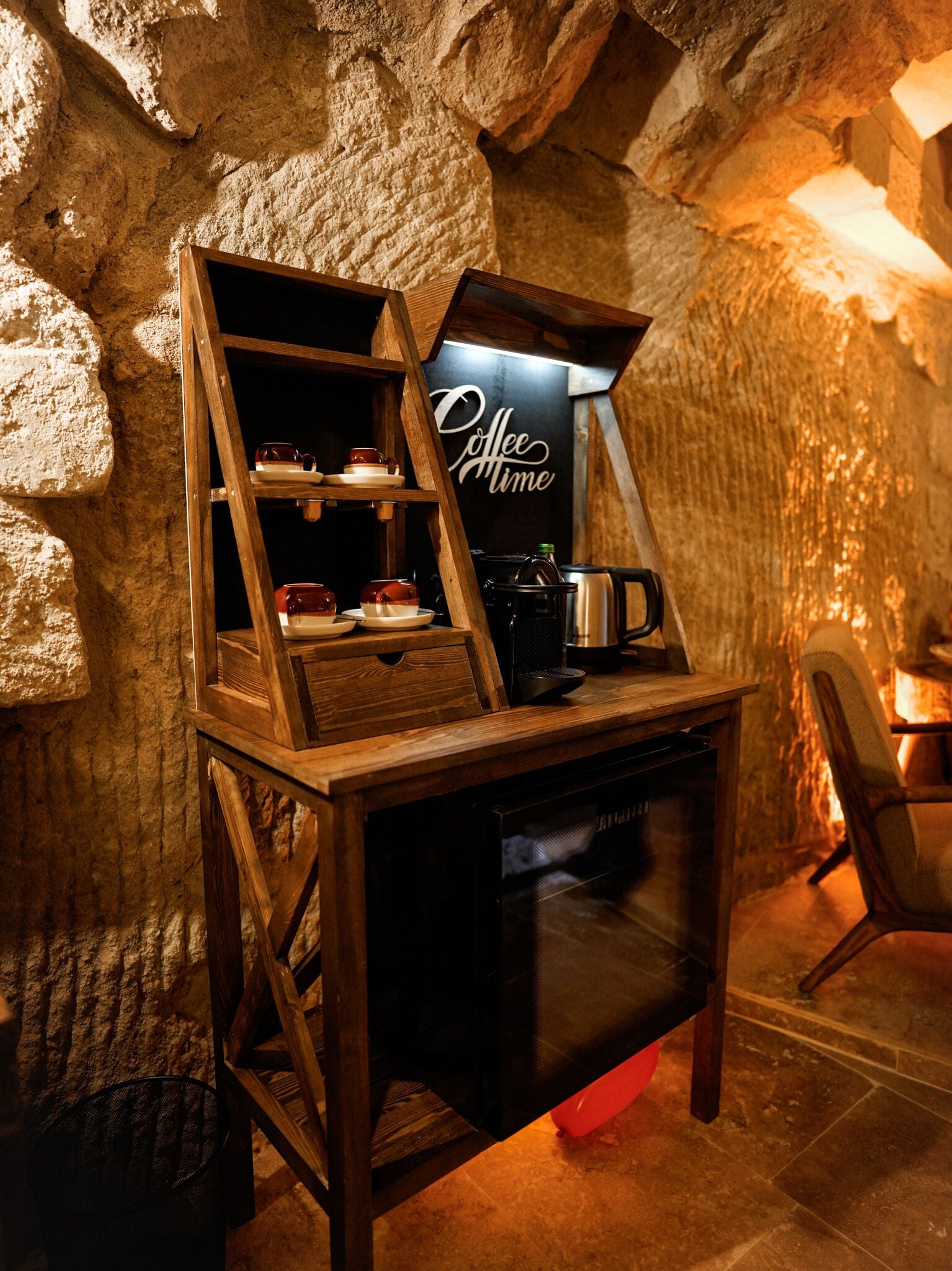 Eine Kaffeestation mit einer Holzregaleinrichtung, einer Kaffeemaschine und einem Schild mit der Aufschrift 'Coffee Time' in einem Raum mit Steinwänden.