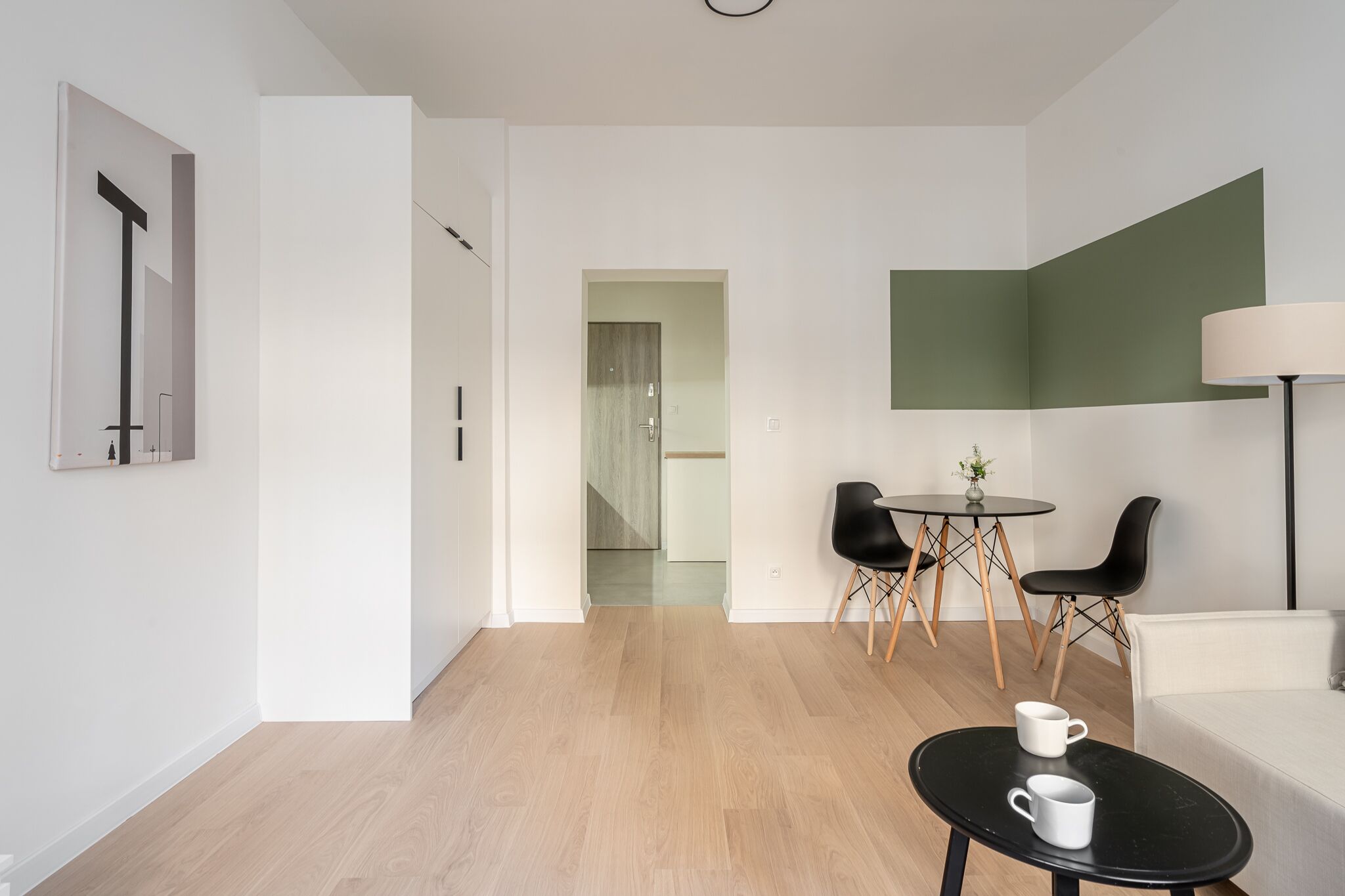 A modern, minimalist room with a wooden floor, a round dining table with chairs, a white sofa, and a lamp.