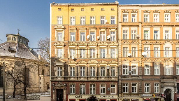 Ein mehrstöckiges Gebäude mit einem Café im Erdgeschoss, einer Kirche mit Kuppel und mehreren parkenden Autos.